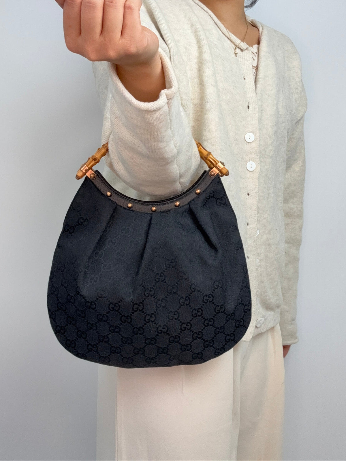 Gucci bag in black GG canvas with studded detailing and a bamboo handle. On Model Elbow 2