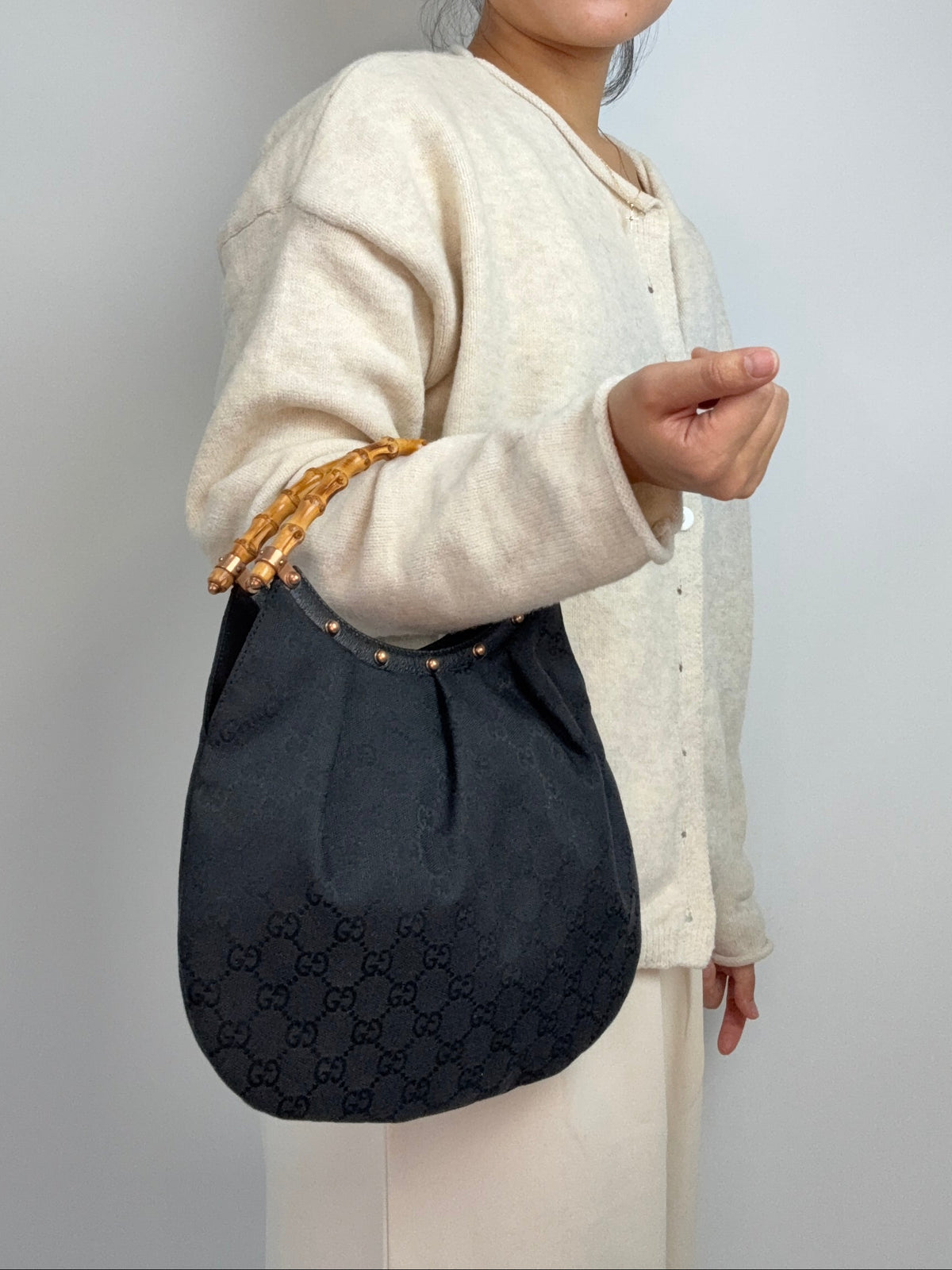 Gucci bag in black GG canvas with studded detailing and a bamboo handle. On Model Elbow
